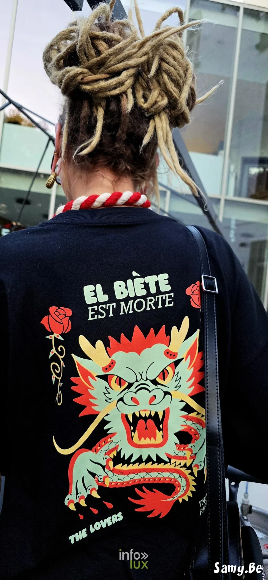 Personne de dos portant un t-shirt noir à motif de dragon et un cordon rouge et blanc au Doudou de Mons